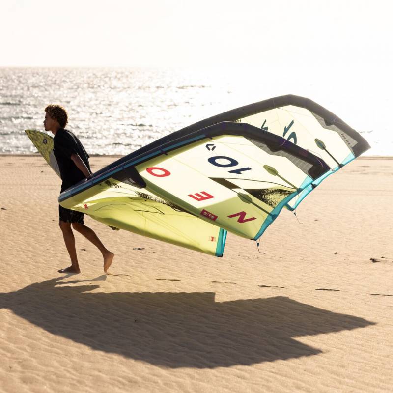 Kitesurfeur portant une aile Duotone Neo SLS 2025 sur la plage face à la mer
