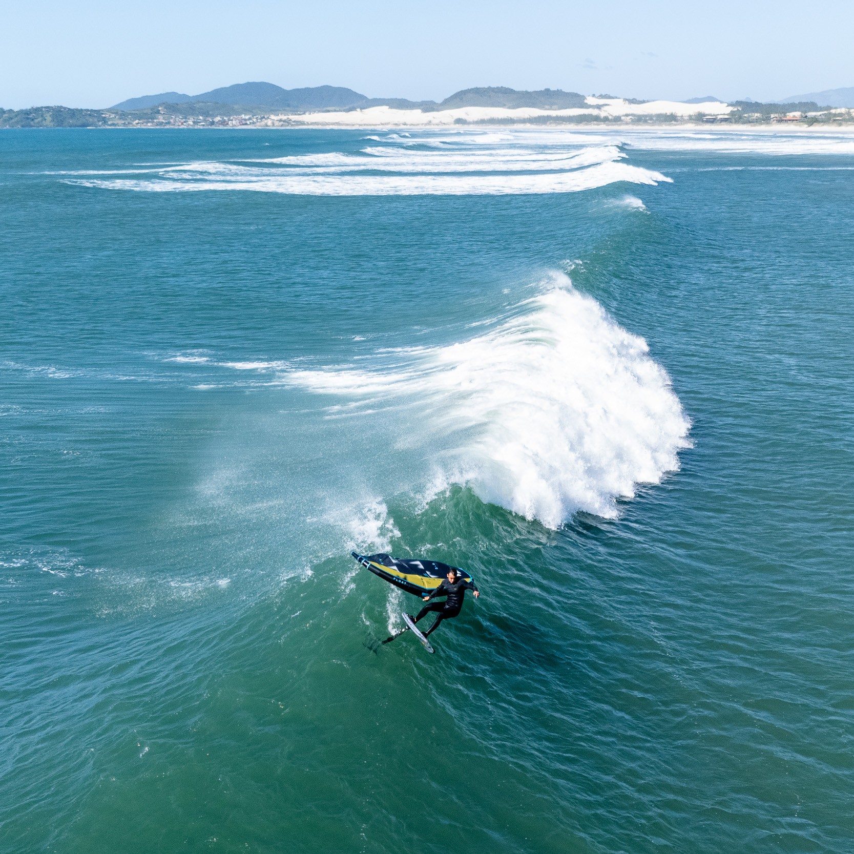 Rider en wingfoil utilisant une aile DUOTONE Float sur une grande vague, exécutant un virage engagé avec foil, conditions parfaites en mer ouverte