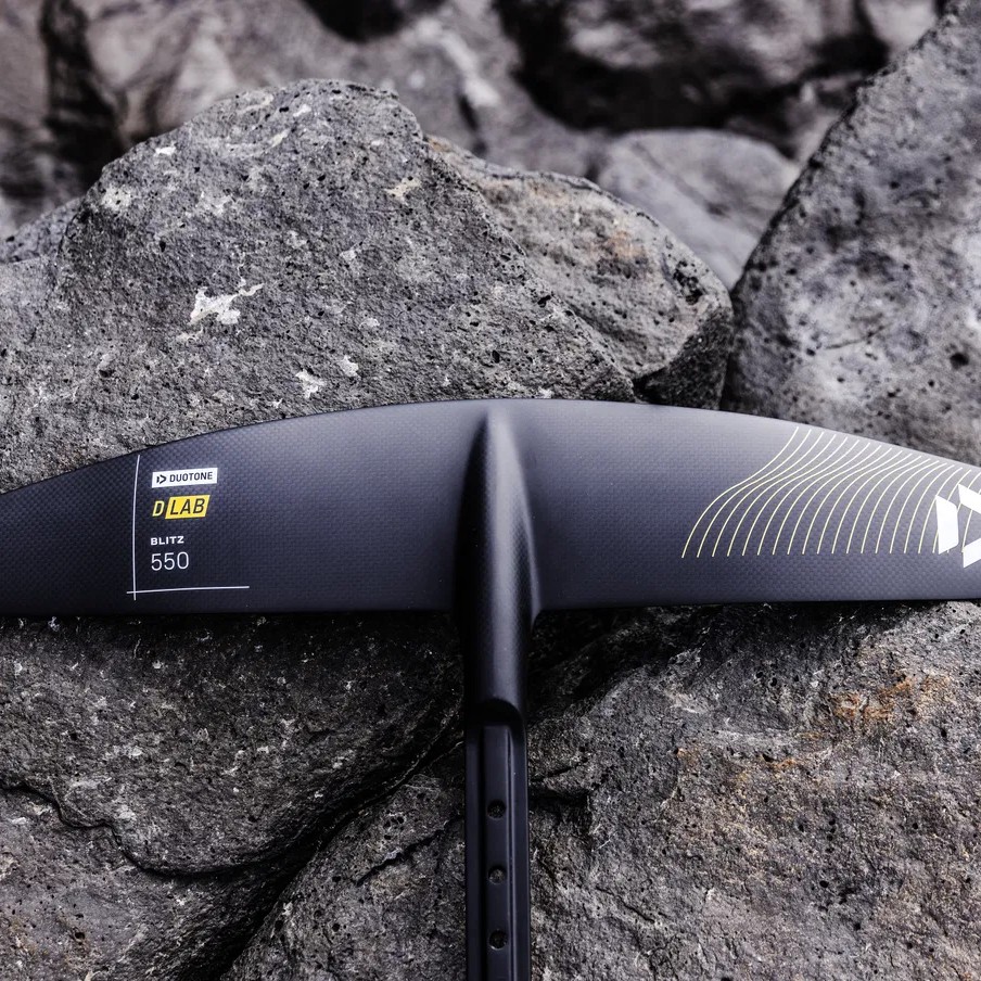 Aile avant Duotone Blitz D/LAB 550 posée sur roche, finition carbone haut de gamme pour foil wingfoil.