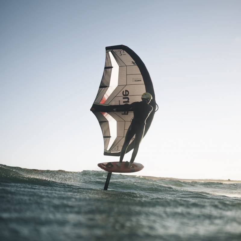 Rider en foil avec la F-ONE Swing V5 noire, en navigation fluide sur plan d’eau calme – aile réactive et compacte pour transitions rapides